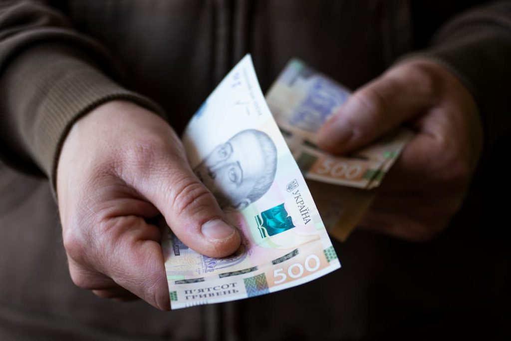 Крупним планом чоловік дає українські грошові купюри.